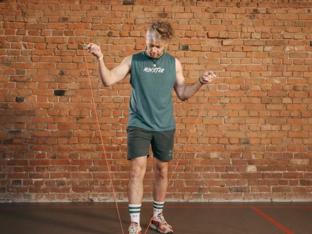 Caucasian man engaging in a jump rope workout in an indoor setting with a brick wall background.