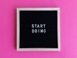 Black letter board with 'Start Doing' motivational text on bright pink background.