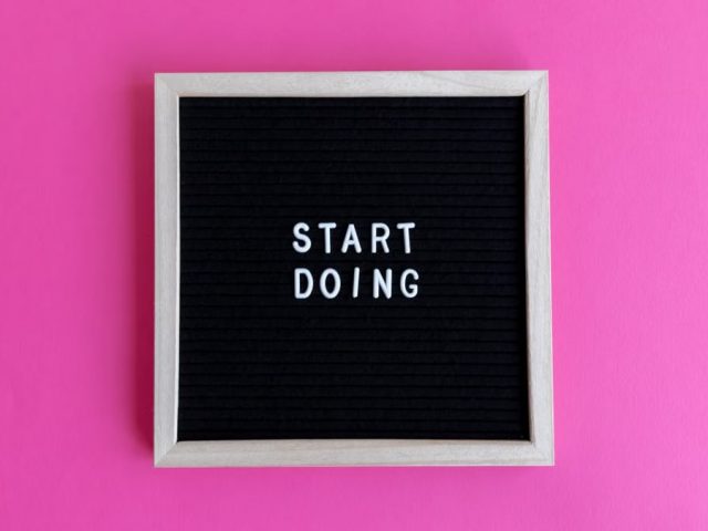 Black letter board with 'Start Doing' motivational text on bright pink background.